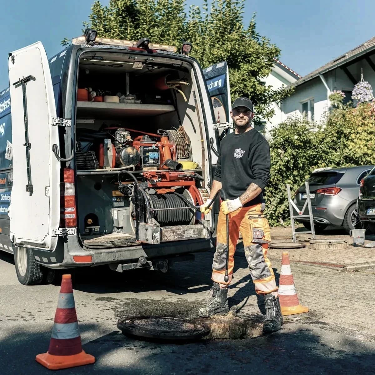 Monteur von Menke Umweltdienste am abgesicherten Schacht mit geöffnetem Einsatzfahrzeug