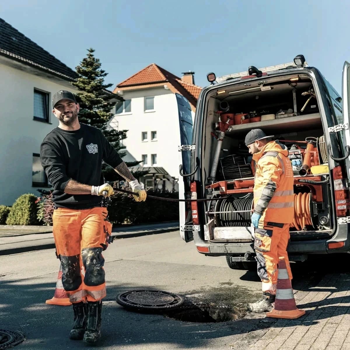 Zwei Monteure von Menke Umweltdienste am geöffneten Schacht mit dem Einsatzfahrzeug